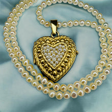 Load image into Gallery viewer, May include: A gold heart-shaped locket pendant adorned with small pearls, suspended from a double strand of creamy-white pearl necklace. The locket features a textured gold surface and a central heart motif composed of densely clustered pearls. The necklace is elegantly draped, showcasing the pendant's intricate details and the lustrous sheen of the pearls.
